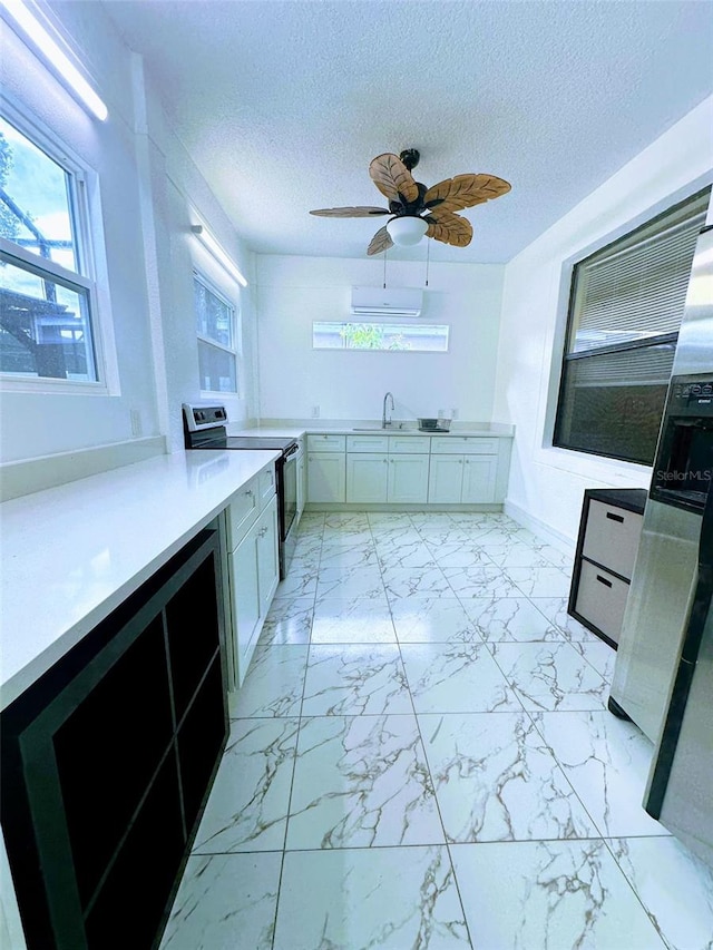 kitchen with ceiling fan, sink, a textured ceiling, stainless steel range with electric stovetop, and white cabinets