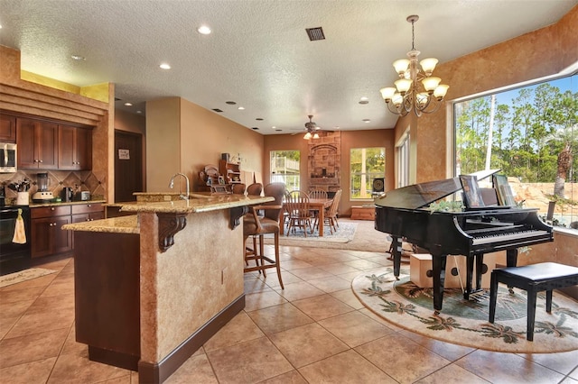 interior space with ceiling fan with notable chandelier, light tile patterned floors, a textured ceiling, decorative light fixtures, and light stone counters