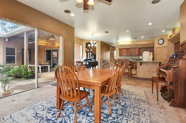 dining room with ceiling fan with notable chandelier, light colored carpet, and a textured ceiling