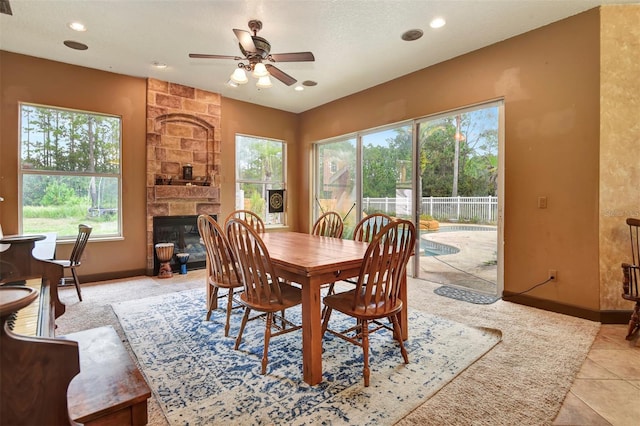 tiled dining space with a textured ceiling, a stone fireplace, and ceiling fan