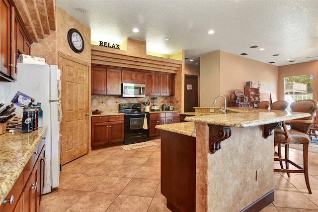 kitchen with light stone countertops, a textured ceiling, a kitchen island with sink, black electric range, and a breakfast bar area