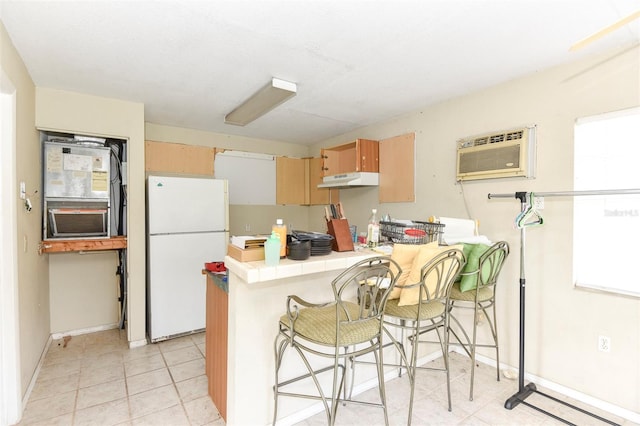 kitchen with a wall mounted air conditioner, white refrigerator, a baseboard radiator, kitchen peninsula, and a breakfast bar area