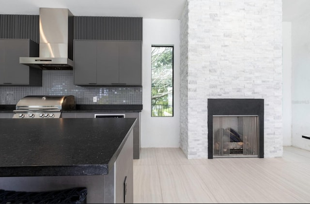 kitchen with a stone fireplace, decorative backsplash, light tile patterned floors, and wall chimney range hood