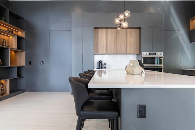 kitchen with decorative light fixtures, gray cabinets, light tile patterned flooring, and a breakfast bar area