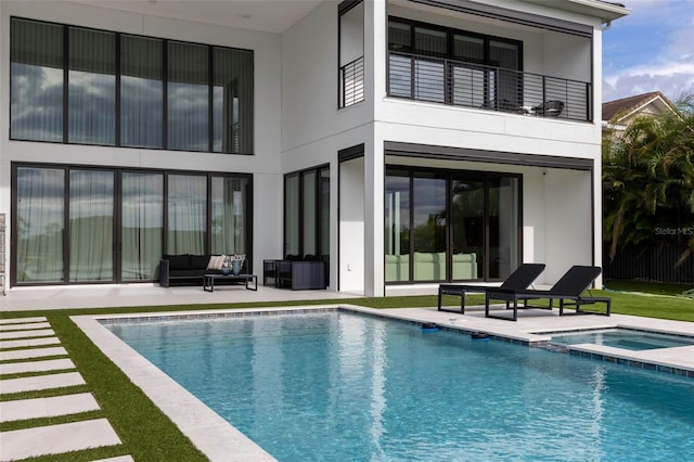 back of house with outdoor lounge area, a pool with hot tub, a balcony, and a patio