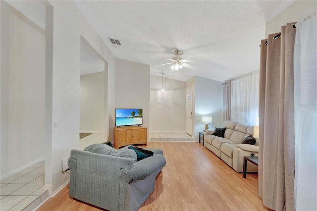 living room featuring ceiling fan, light hardwood / wood-style floors, and a textured ceiling