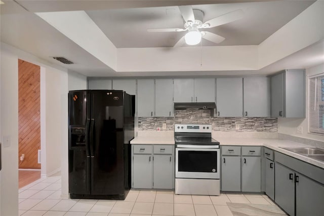 kitchen featuring light tile patterned floors, a tray ceiling, black fridge, and electric stove