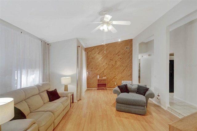 living room with wooden walls, ceiling fan, and light wood-type flooring