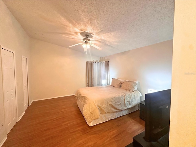 bedroom featuring a textured ceiling, ceiling fan, dark wood-type flooring, and two closets