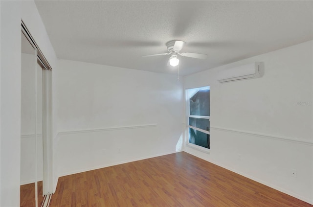 empty room featuring a wall mounted air conditioner, ceiling fan, a textured ceiling, and hardwood / wood-style flooring