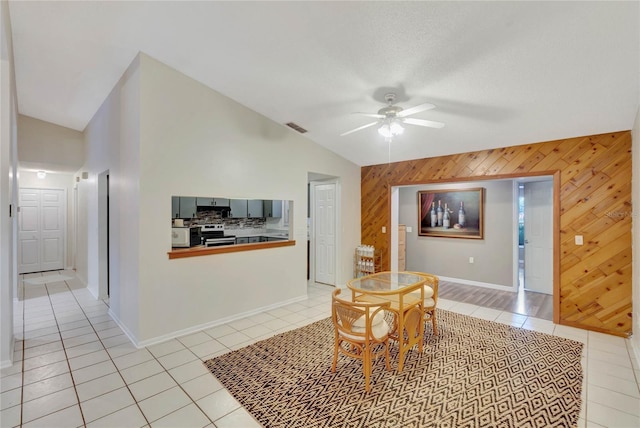 tiled dining area featuring ceiling fan, lofted ceiling, and wooden walls