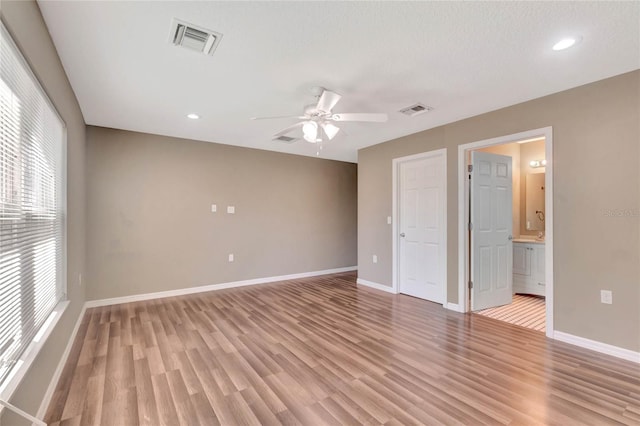 empty room featuring plenty of natural light, ceiling fan, light wood-type flooring, and a textured ceiling