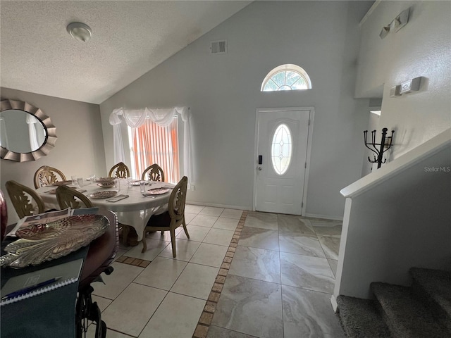 tiled foyer entrance with a textured ceiling and high vaulted ceiling