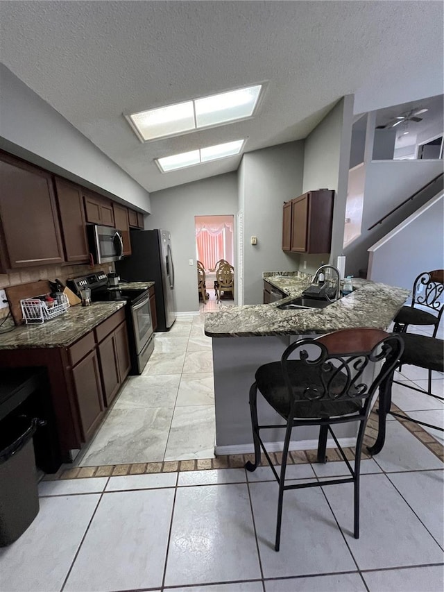 kitchen with kitchen peninsula, stainless steel appliances, sink, lofted ceiling, and a breakfast bar area