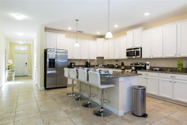 kitchen with appliances with stainless steel finishes, a center island with sink, pendant lighting, and dark stone countertops