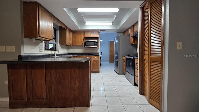 kitchen with a raised ceiling, sink, light tile patterned floors, appliances with stainless steel finishes, and kitchen peninsula