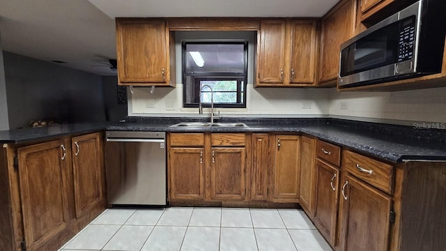 kitchen with dark stone countertops, sink, light tile patterned floors, and stainless steel appliances