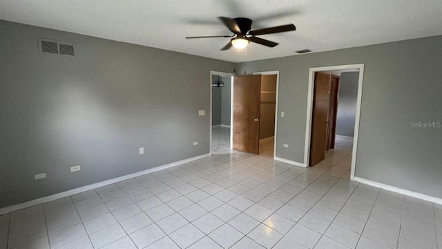 unfurnished bedroom with ceiling fan, light tile patterned flooring, a walk in closet, and a textured ceiling