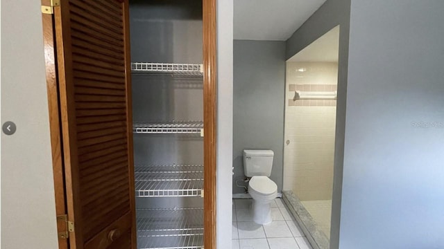 bathroom featuring tile patterned flooring, tiled shower, and toilet