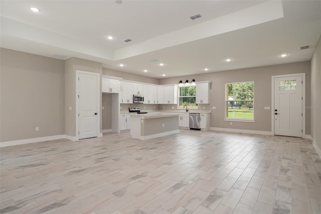 kitchen featuring appliances with stainless steel finishes, light wood-type flooring, a kitchen island, sink, and white cabinetry