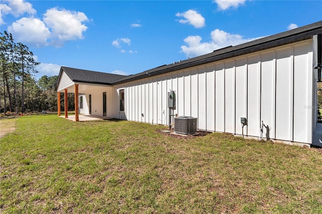 rear view of house with board and batten siding, a patio area, a lawn, and central AC