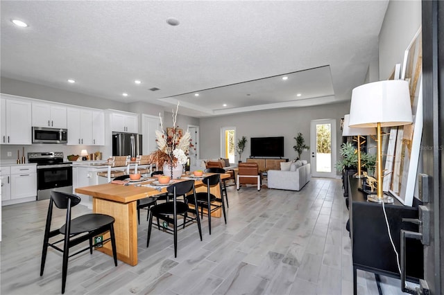 dining room featuring visible vents, a raised ceiling, a textured ceiling, light wood-style floors, and recessed lighting