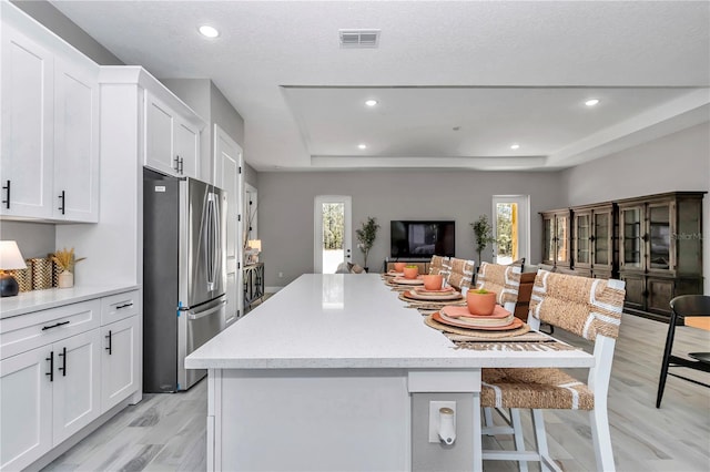 kitchen with visible vents, a raised ceiling, a breakfast bar area, freestanding refrigerator, and white cabinetry