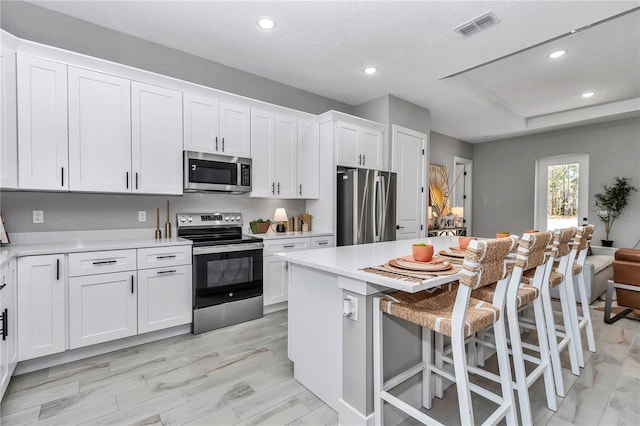 kitchen with stainless steel appliances, light countertops, visible vents, white cabinets, and a kitchen bar