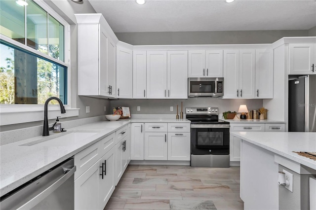 kitchen with white cabinets, light stone counters, appliances with stainless steel finishes, a textured ceiling, and a sink