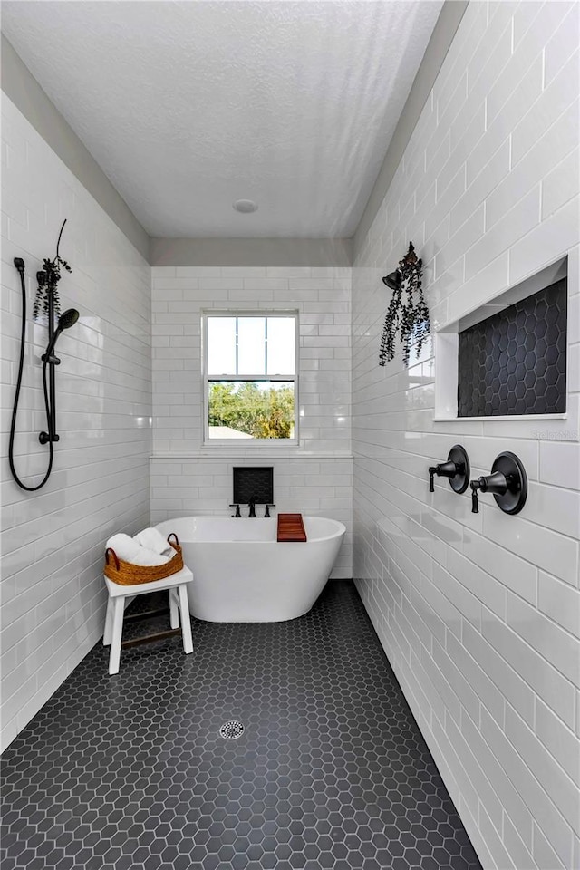 bathroom with a freestanding bath, tiled shower, a textured ceiling, and tile walls