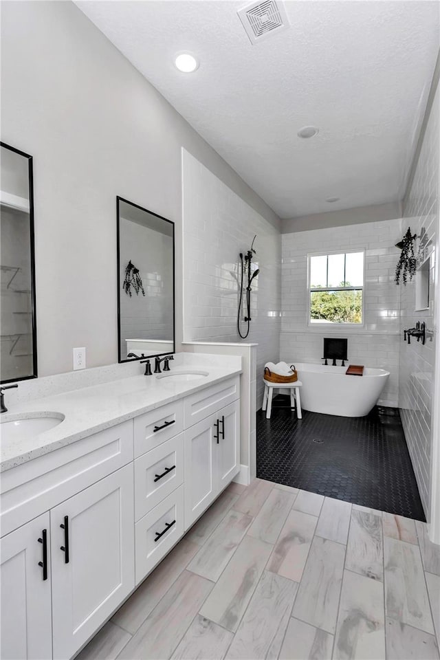 full bathroom with a soaking tub, visible vents, a sink, and double vanity