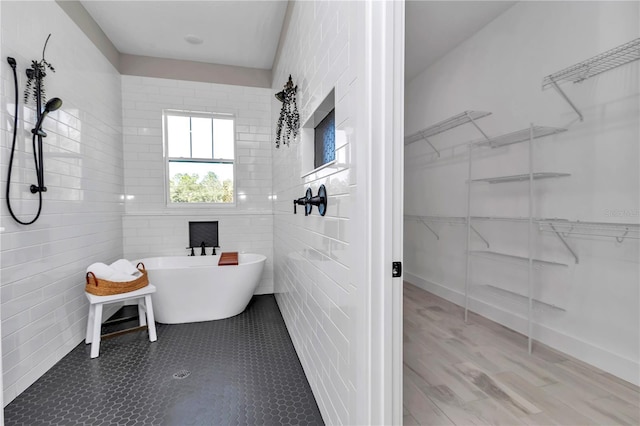 bathroom featuring a walk in closet, a freestanding bath, tile walls, and tile patterned floors