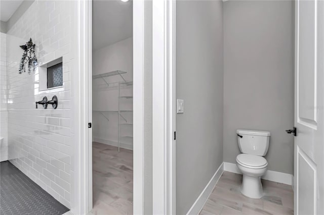 bathroom with toilet, baseboards, walk in shower, and a walk in closet