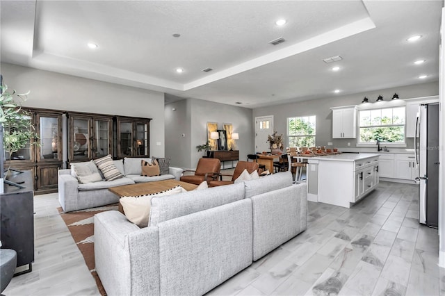 living area with a raised ceiling, visible vents, and recessed lighting