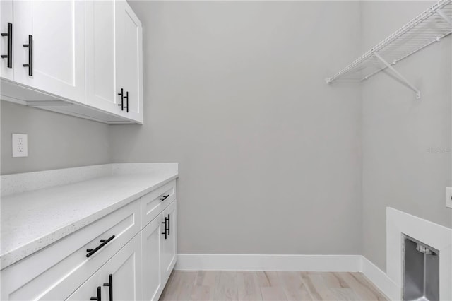 clothes washing area featuring light wood-type flooring, cabinet space, and baseboards