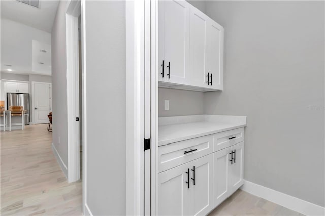 bar with light wood-style floors, freestanding refrigerator, and baseboards