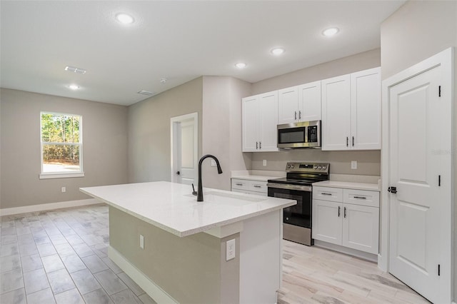 kitchen with appliances with stainless steel finishes, light wood-type flooring, sink, white cabinetry, and an island with sink