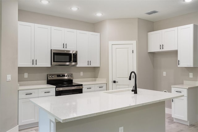 kitchen with appliances with stainless steel finishes, light stone counters, white cabinetry, and an island with sink