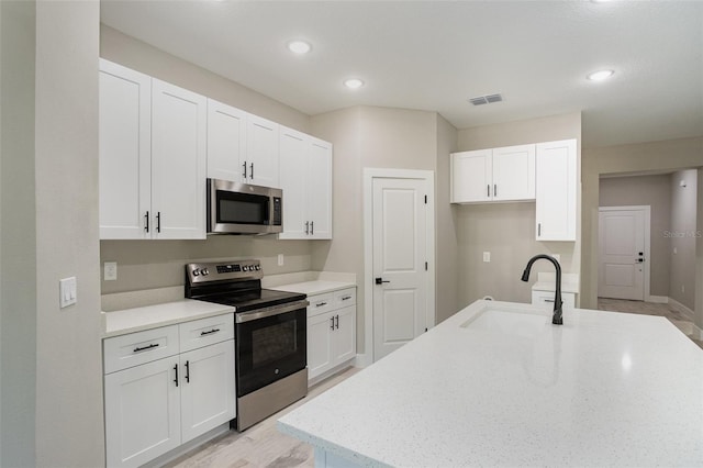 kitchen with light stone countertops, stainless steel appliances, white cabinetry, and sink