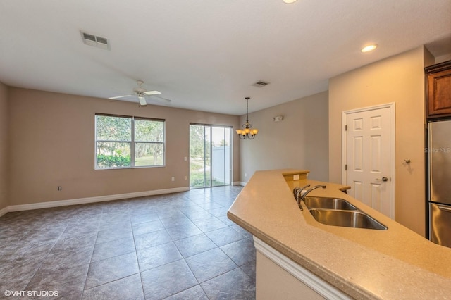 kitchen with ceiling fan with notable chandelier, sink, pendant lighting, light tile patterned floors, and stainless steel refrigerator