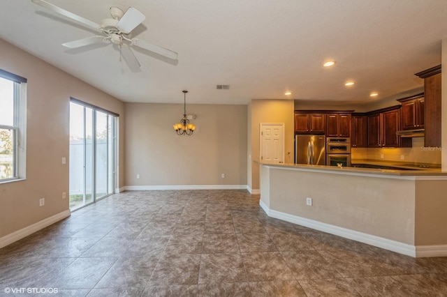 kitchen with pendant lighting, ceiling fan with notable chandelier, kitchen peninsula, appliances with stainless steel finishes, and dark brown cabinetry