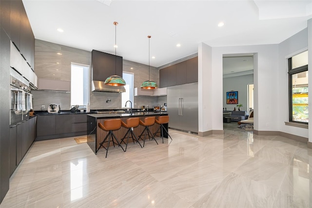 kitchen featuring pendant lighting, a kitchen breakfast bar, sink, wall chimney exhaust hood, and appliances with stainless steel finishes