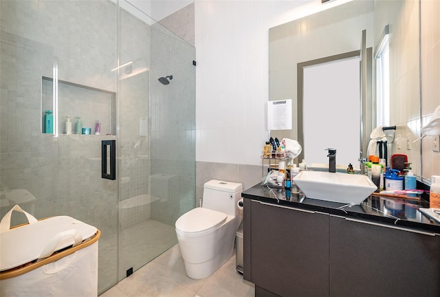 bathroom featuring vanity, a shower with door, tile patterned floors, toilet, and tile walls