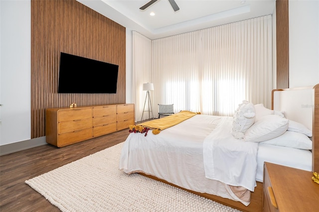 bedroom featuring ceiling fan, dark wood-type flooring, and a tray ceiling