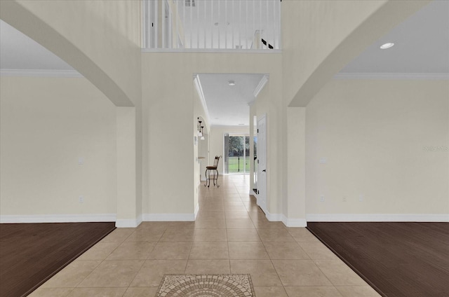 hallway with crown molding, a towering ceiling, and light wood-type flooring