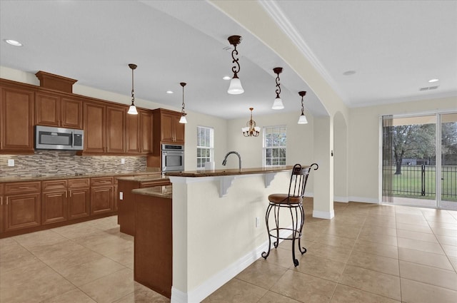 19206 Robertson St, Orlando, FL 32833 - kitchen with appliances with stainless steel finishes, an island with sink, brown cabinetry, decorative backsplash, and ornamental molding