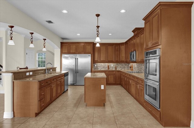 19206 Robertson St, Orlando, FL 32833 - kitchen with an island with sink, stainless steel appliances, brown cabinetry, light stone counters, and backsplash