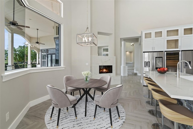 dining room featuring ceiling fan, sink, a towering ceiling, light parquet floors, and a fireplace