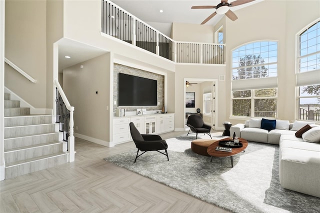 living room with ceiling fan, light parquet floors, and a towering ceiling