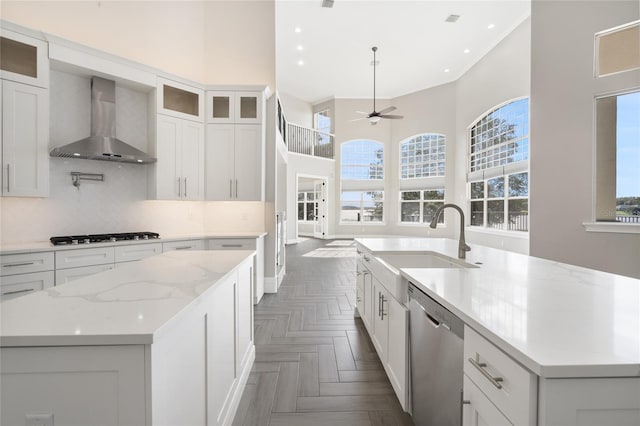 kitchen with appliances with stainless steel finishes, a kitchen island with sink, sink, wall chimney range hood, and white cabinetry